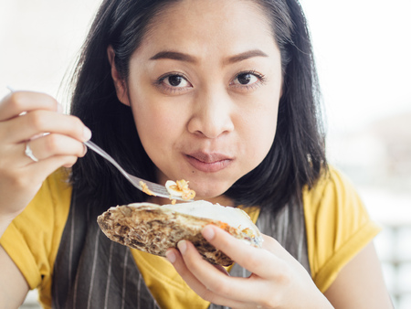 Asian woman eats Thai style fresh oyster with garlic.