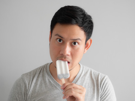 Head shot of Asian man eats ice pop with funny face.の写真素材