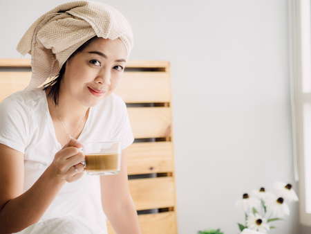 Close up of Asian woman drink morning coffee and relax on her bed after shower.の写真素材