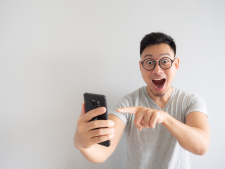 Wow face of Asian man shocked what he see in the smartphone on isolated grey background.