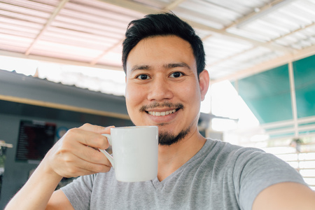 Selfie portrait of happy Asian man drink mug of hot coffee.の写真素材