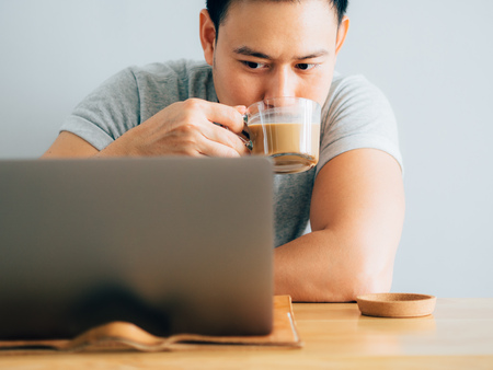 Happy asian man drink coffee while use laptop.