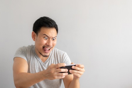 Crazy and funny face of Asian man addicted to play mobile game.