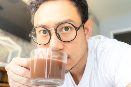 Happy asian man with eyeglasses and white shirt selfy himself drink hot coffee.の写真素材