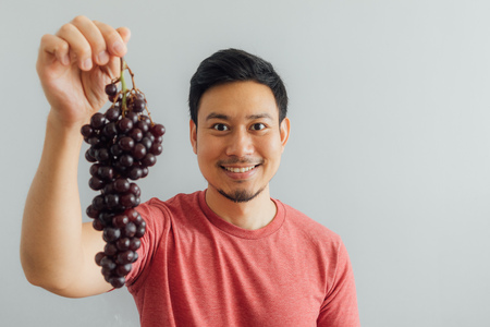 Funny Asian man shows bunch of red grapes.