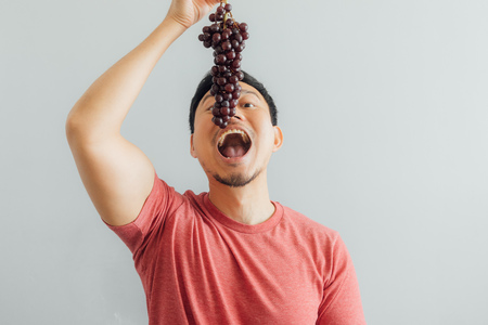 Funny Asian man tries to eat bunch of red grapes.