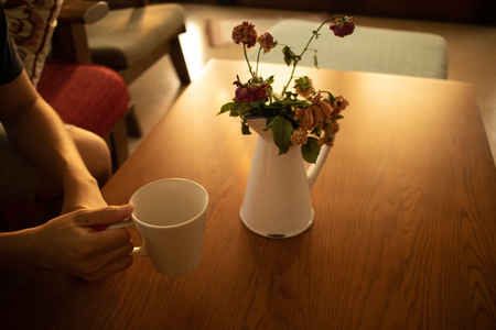 Having a cup of coffee in warmth morning light with flowers vase on the table.の写真素材