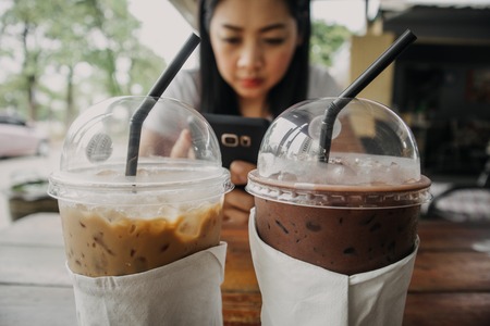 Iced coffee and cocoa drink in plastic cup on wooden table.