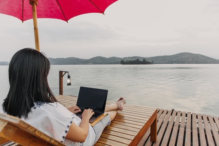 Asian woman work on her laptop and admire the beautiful lake.