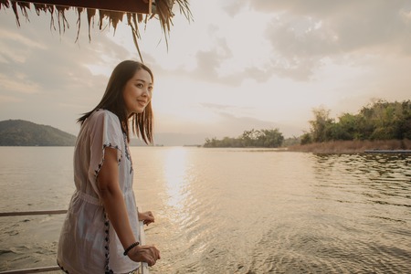 Asian woman tourist admire the beautiful nature of the lake with warm sunset sky.の写真素材