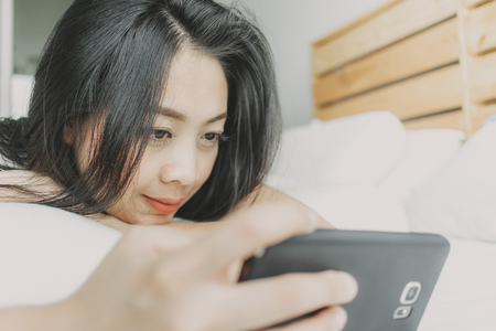 Close up of happy woman use smartphone and relax on her bed.の写真素材