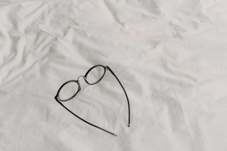 Eyeglasses with black plastic temple on white bed sheet. Concept of read and relax.