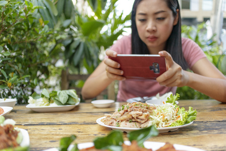Asian woman is taking a photo of Thai food on the table.
