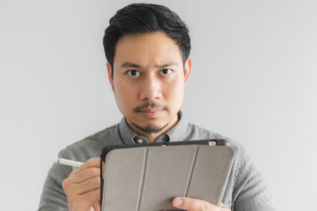 Serious and thinking Asian entrepreneur businessman work on his tablet with grey background.の写真素材
