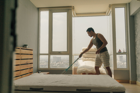 Asian man is cleaning his bedroom with warm summer light in his apartment.の写真素材