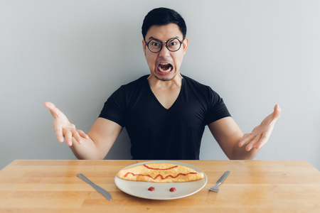 Angry and mad face of Asian man is eating homemade breakfast set of omelet.の写真素材