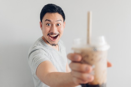 Happy Asian man is drinking Bubble Milk Tea or Pearl Milk Tea. Popular Milk Tea in Asia and Taiwan.の写真素材
