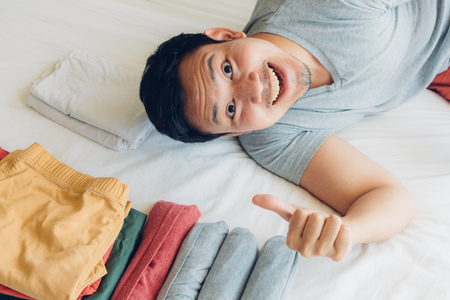 Asian man has finished folding all of his clothes on the bed.の写真素材