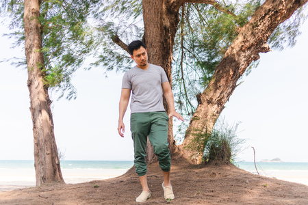 Asian man is standing under the pine tree on the beach. Concept of relaxing outdoor.の写真素材