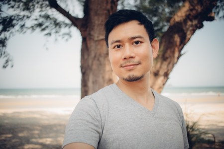 Close up of Asian man is standing under the pine tree on the beach. Concept of relaxing outdoor.の写真素材