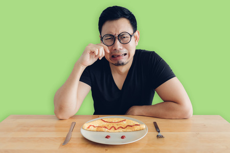 Hate and crying Asian man is eating homemade breakfast set of omelet.の写真素材