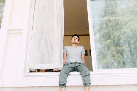 Asian man sit and relax at the front door of the house in summer. Concept of single man life.の写真素材