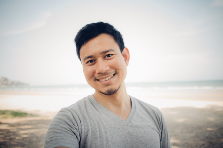 Close up of Asian man is standing under the pine tree on the beach. Concept of relaxing outdoor.