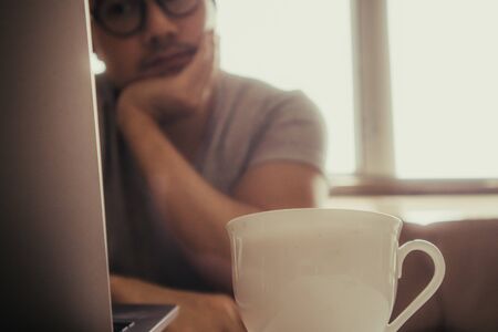 Close up of white cup of hot coffee on the table of a freelance man.