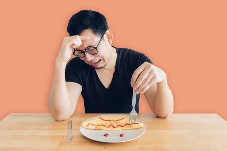 Hate and crying Asian man is eating homemade breakfast set of omelet.の写真素材