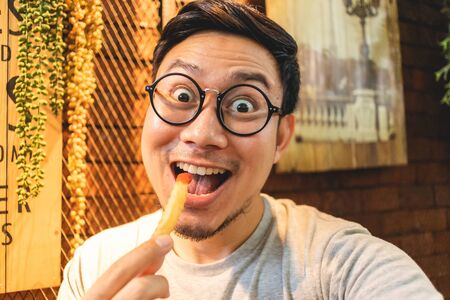 Funny delicious face of Asian man eats French Fries in the cafe.