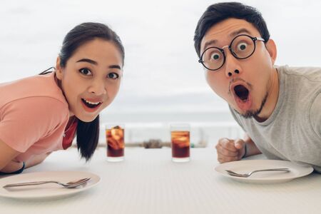 Wow and Shocked face of Asian lover couple having a date at the restaurant on the beach.の写真素材