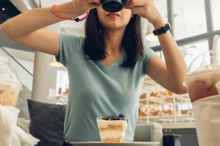 Asian woman is taking a photo of her blueberry cheesecake.
