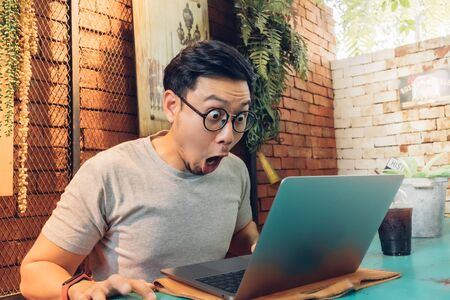 Shocked and surprised face of Asian man works on his laptop in the cafe.の写真素材