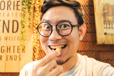 Funny delicious face of Asian man eats French Fries in the cafe.