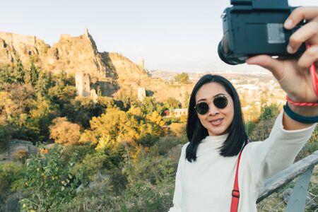 Happy Asian woman tourist is taking selfie shot with Narikala Fortress in Tbilisi, Georgia.