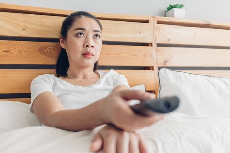 Asian woman is holding a remote control and seriously watching drama tv series.