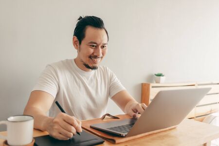 Happy Asian man is working with laptop in his apartment bedroom in concept of Work From Home and Work at Home.の写真素材