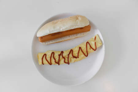 Simple easy breakfast of omelette and sausage served on white dish.の写真素材