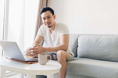 Asian man is working on his laptop in the living room with a cup of coffee.の写真素材