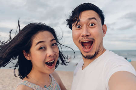 Funny wow face selfie of couple on windy beach.