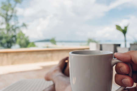 Man drinks coffee on the balcony by the sea in concept of relaxation and vacation.の写真素材