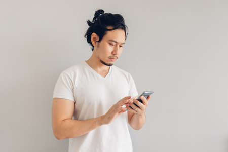 Long hair Asian man in white casual t-shirt is using smartphone.の写真素材