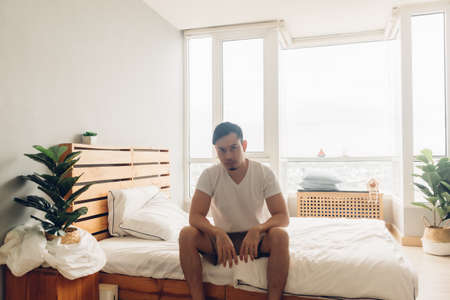 Lonely and depressed Asian man in his bedroom in the apartment.