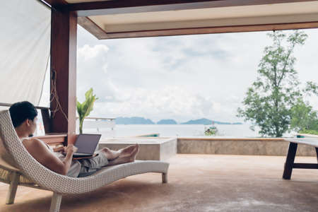 Asian man relax on the bench and working on his laptop with sea view.の写真素材