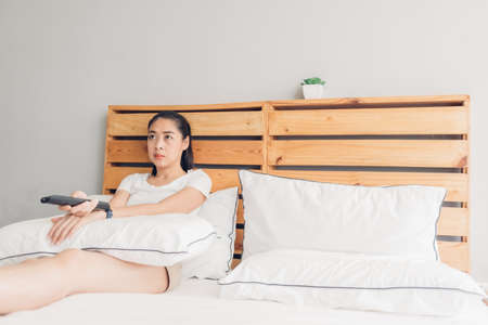 Asian woman is holding a remote control and seriously watching drama tv series.