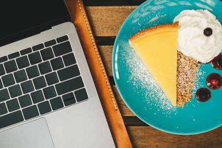 Top view of laptop on the desk with cheesecake on the side. Concept of happy work.