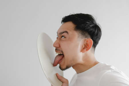 Funny face Asian man is licking white dish in concept of very delicious meal.の写真素材