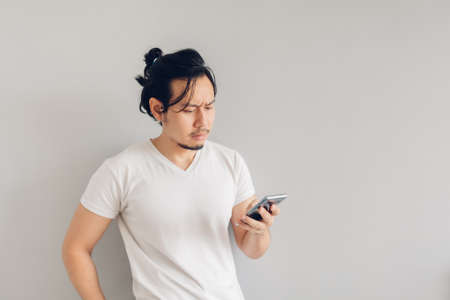 Serious long hair Asian man in white casual t-shirt is using smartphone.の写真素材