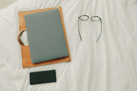 Working set of laptop smartphone and eyeglasses on white bed in bedroom.の写真素材