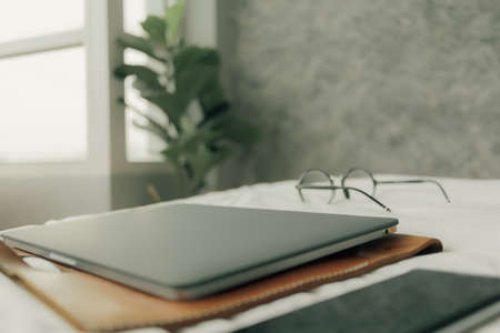 Working set of laptop smartphone and eyeglasses on white bed in bedroom.の写真素材